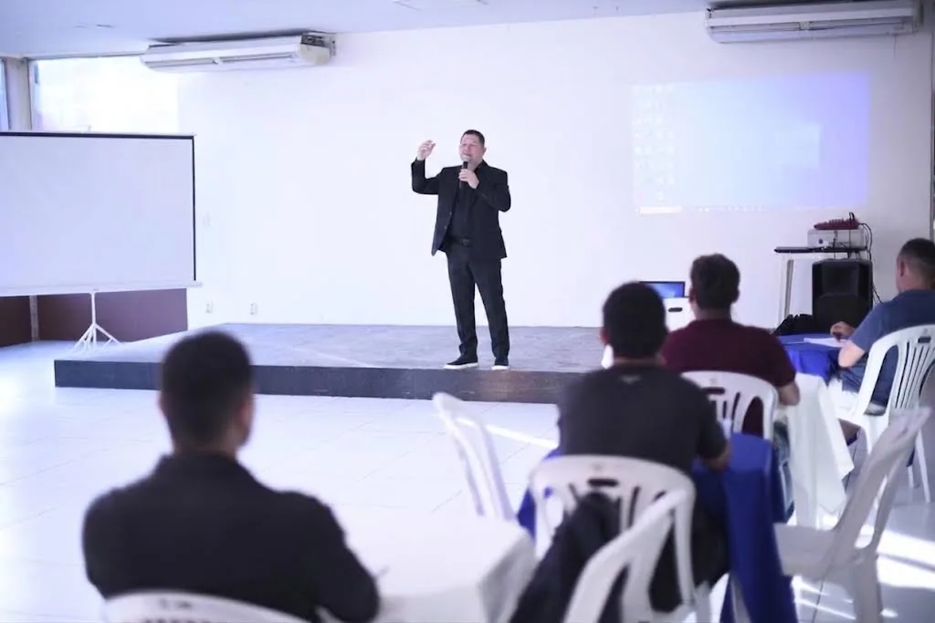 Wendell Souza no palco, ao microfone, diante de uma plateia sentada